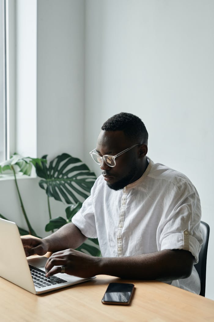 African American man typing on a laptop at a desk in a modern office.