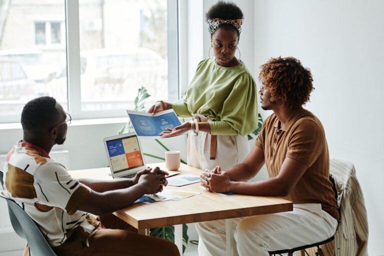 Three colleagues engage in a collaborative meeting, discussing a project in a bright, modern office.