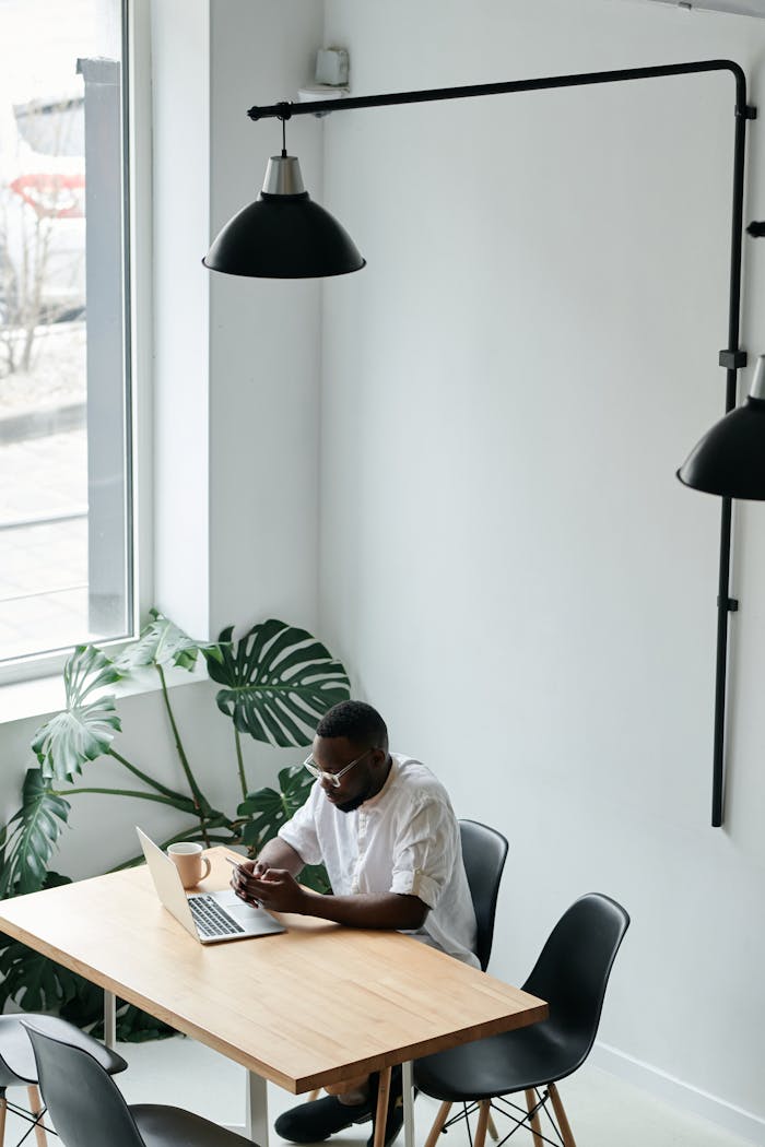 Businessman using laptop in a modern, minimalistic workspace with ample natural light.