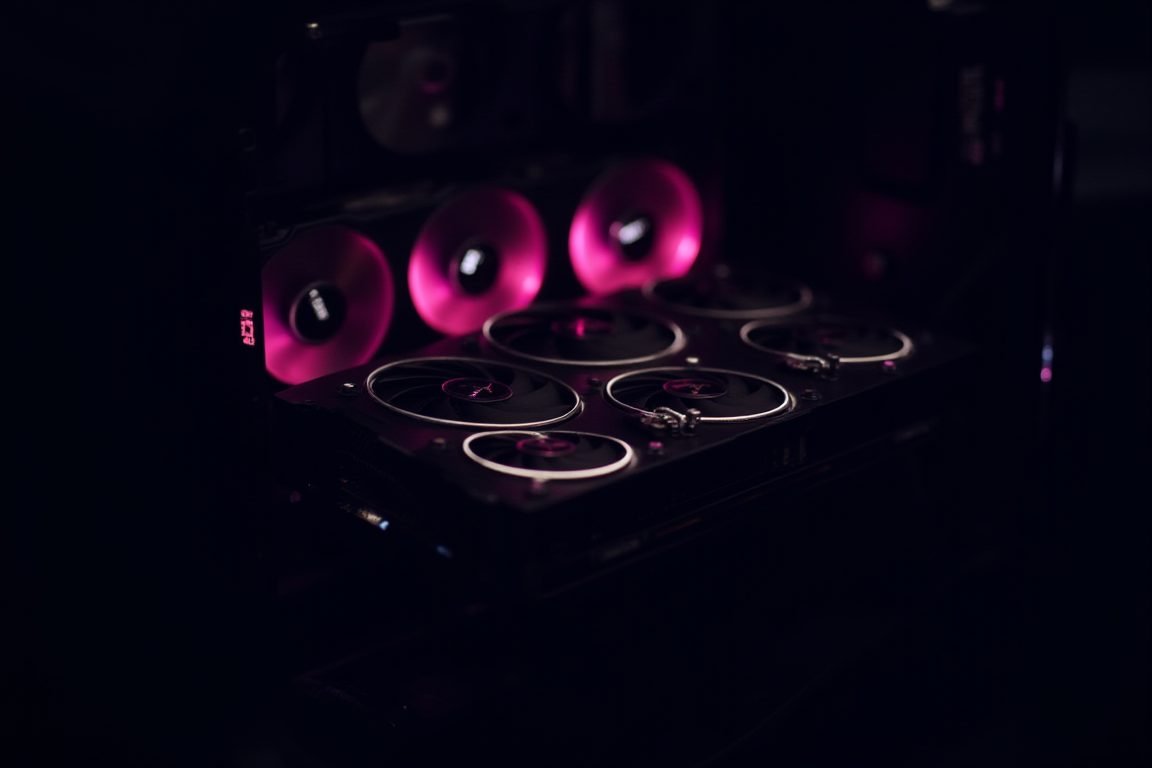 Four professional workstation GPUs installed in an open PC case with glowing fans in a dim room, technical and cinematic phot